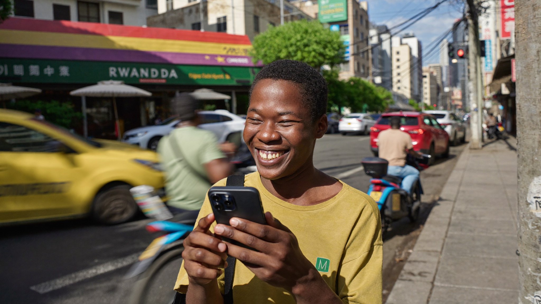 A happy young Rwandan man smiling at a fast-loading website on his smartphone on a busy Kigali street